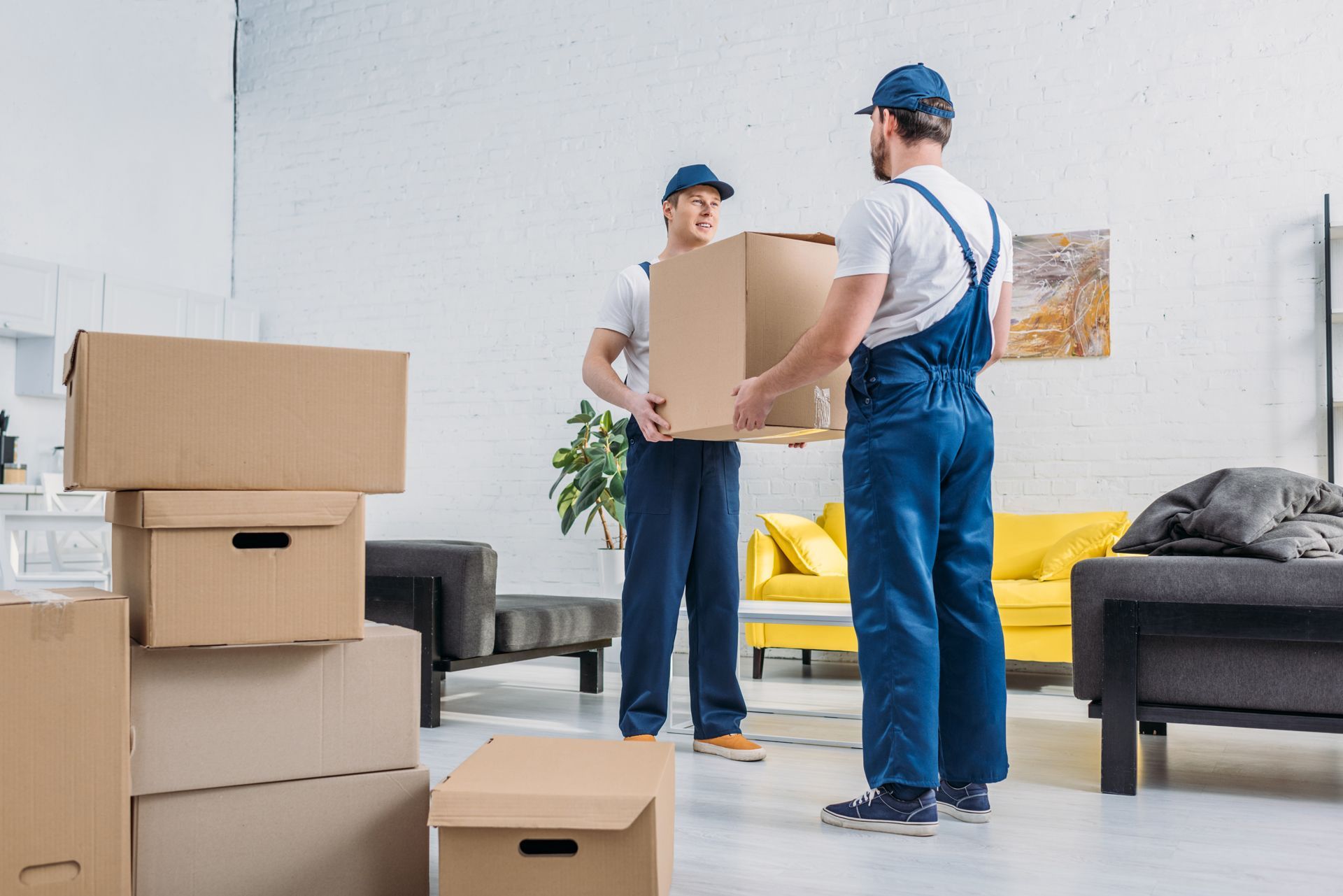 Two men are carrying boxes in a living room.