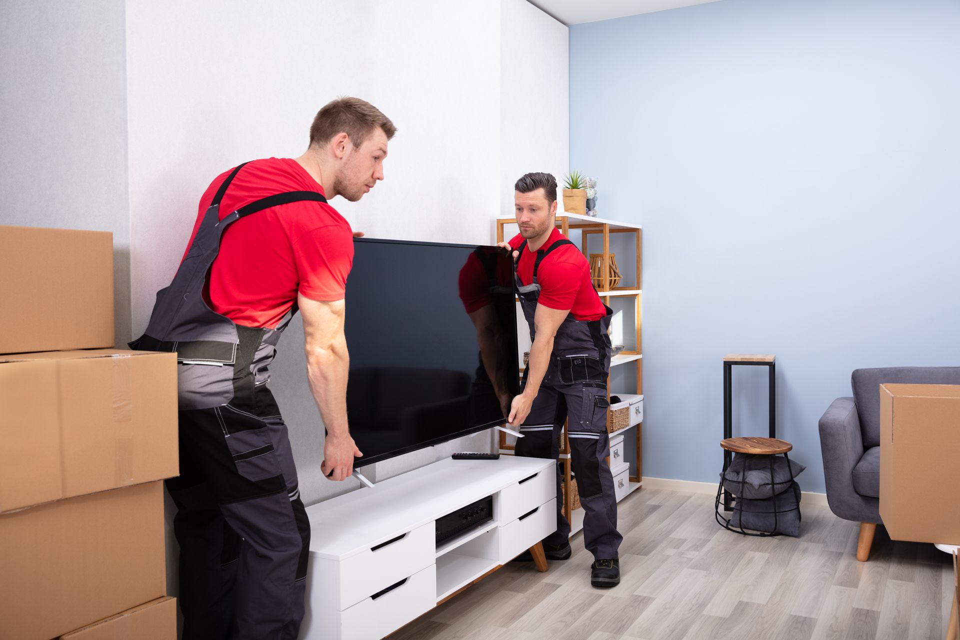 Two men are moving a flat screen tv in a living room.