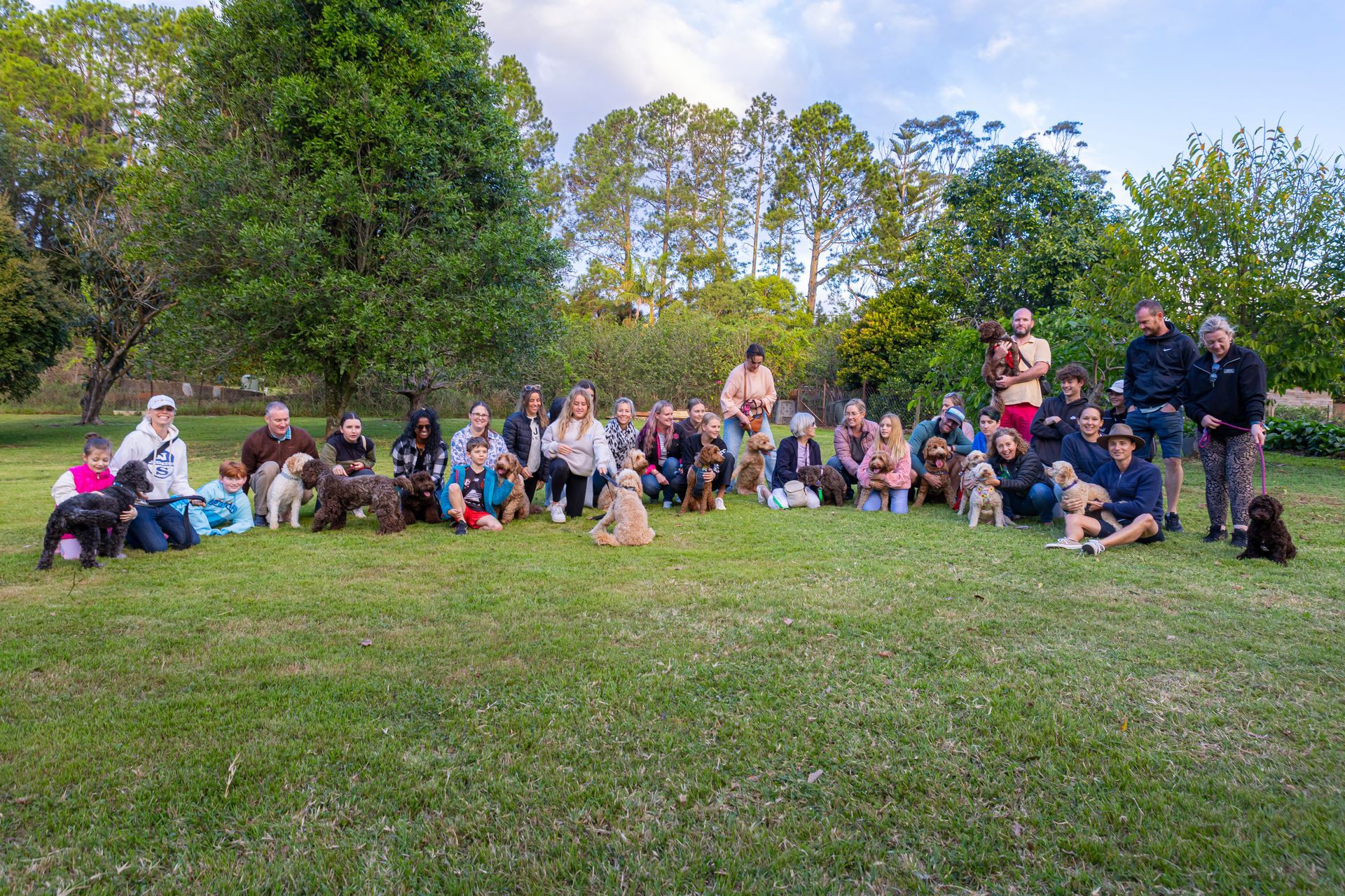A group of people and their dogs are posing for a picture in a park.