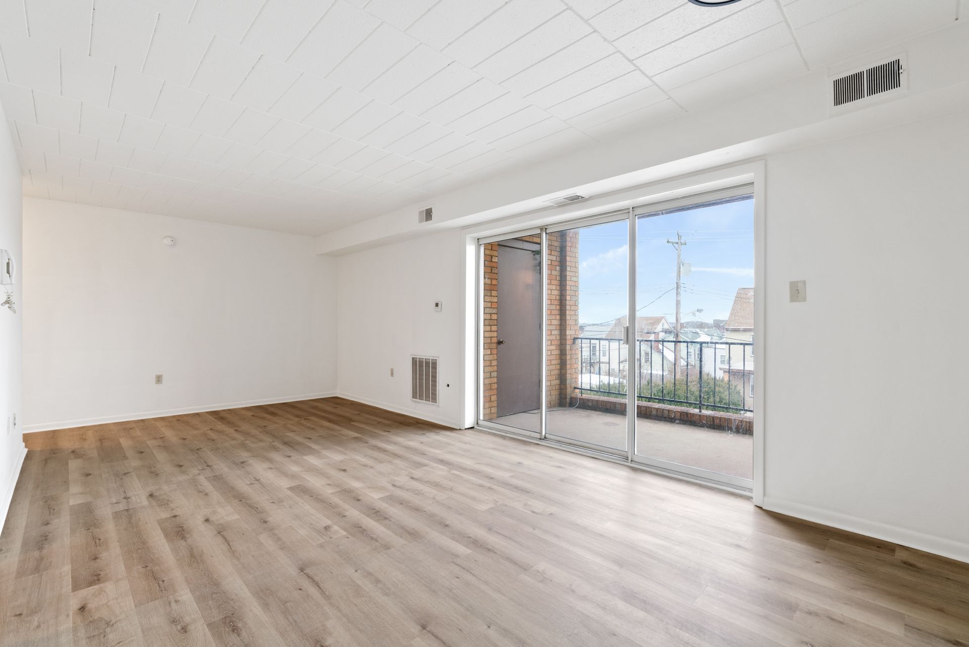 An empty living room with hardwood floors and sliding glass doors leading to a balcony.