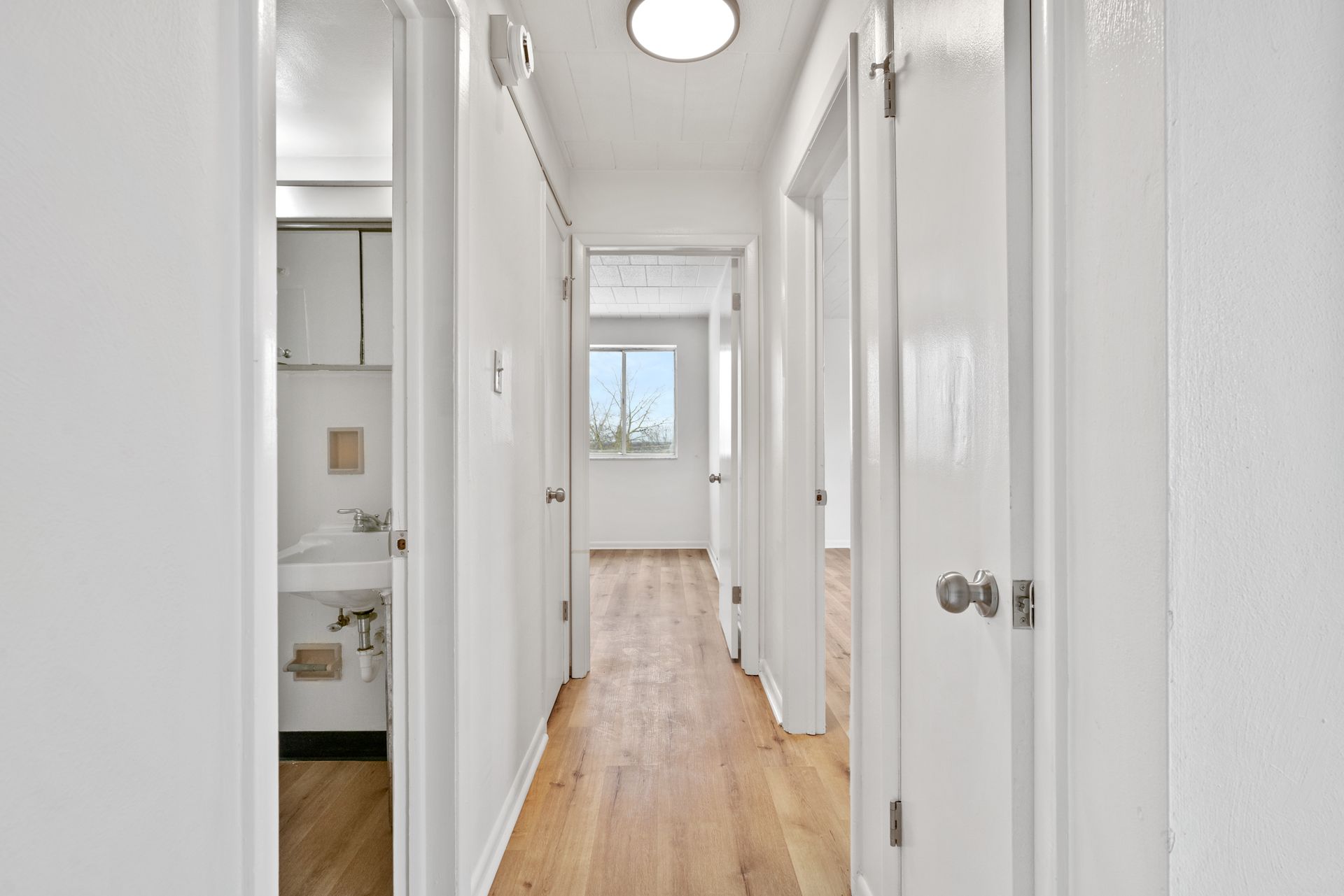 A long hallway with white walls and wooden floors leading to a bathroom.