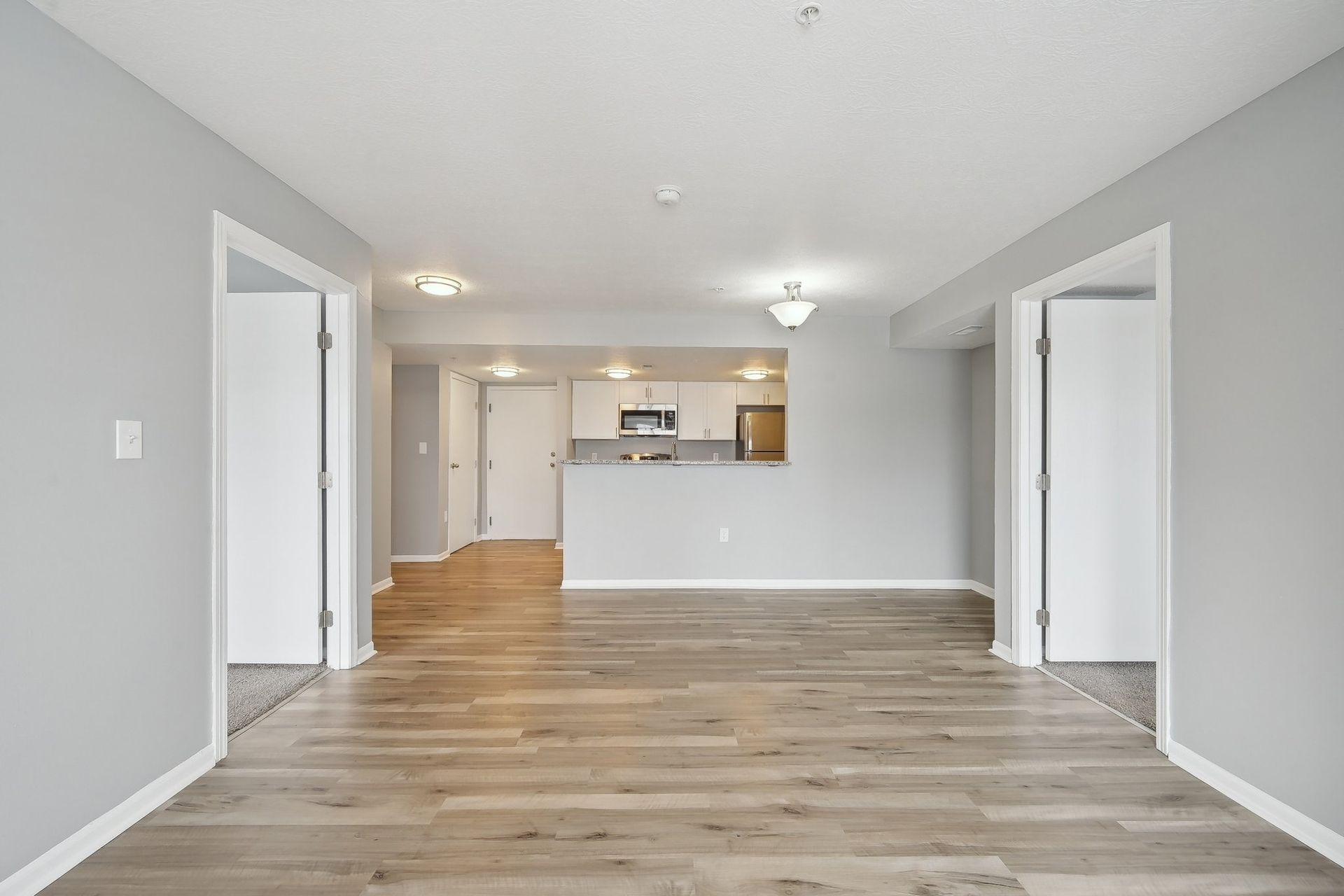 A living room with hardwood floors and a kitchen in the background.