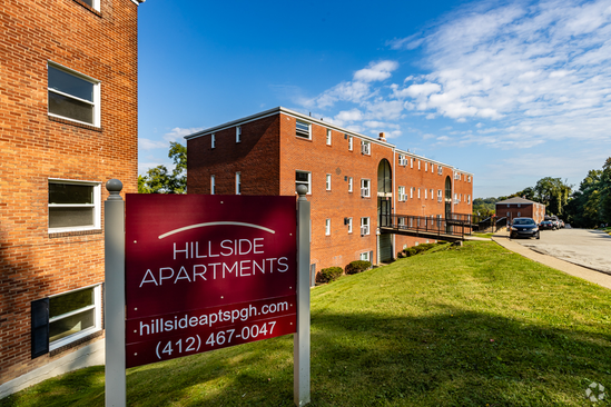 A sign for hillside apartments is in front of a brick building.