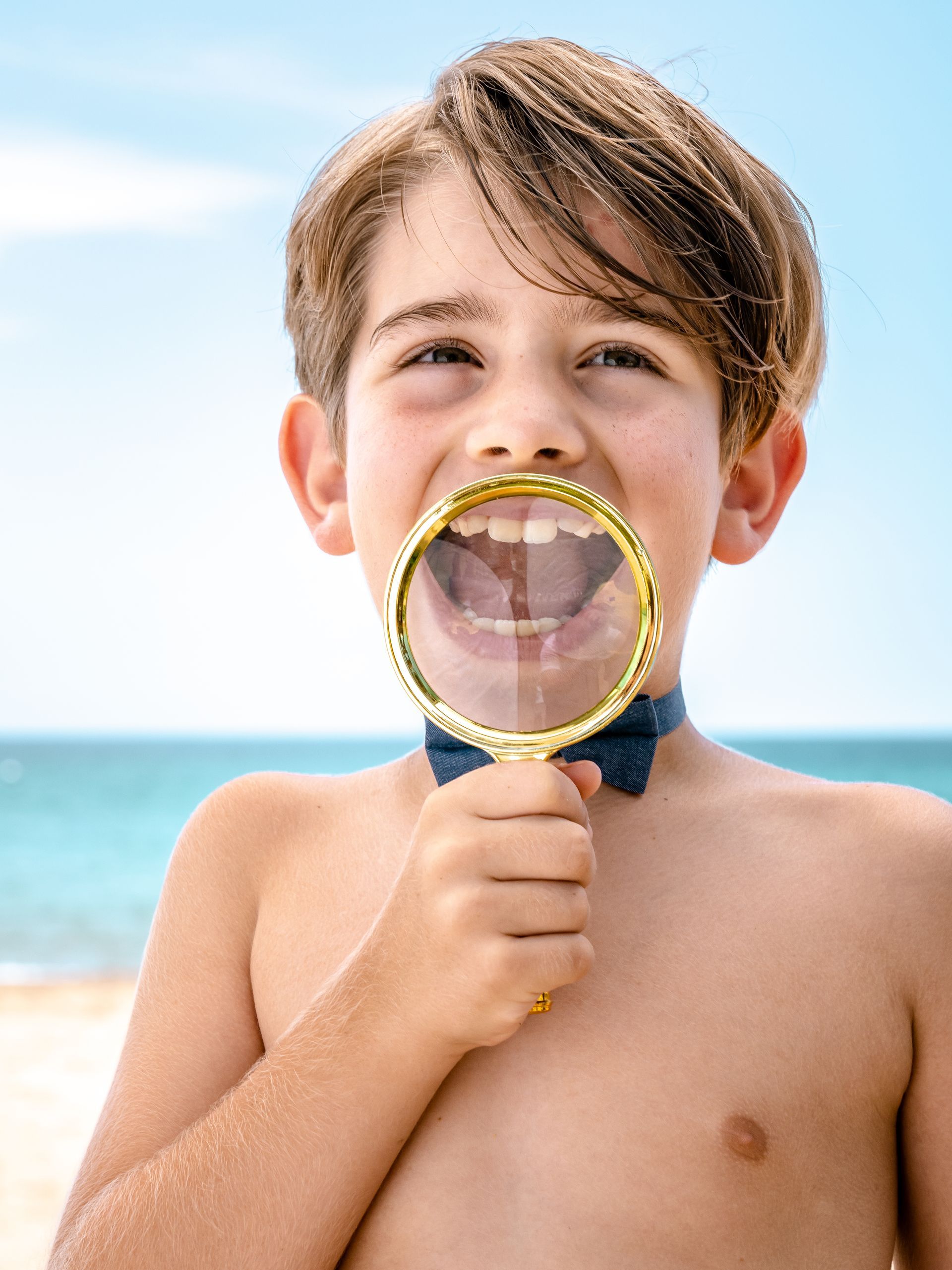 A young boy is holding a magnifying glass in his mouth.