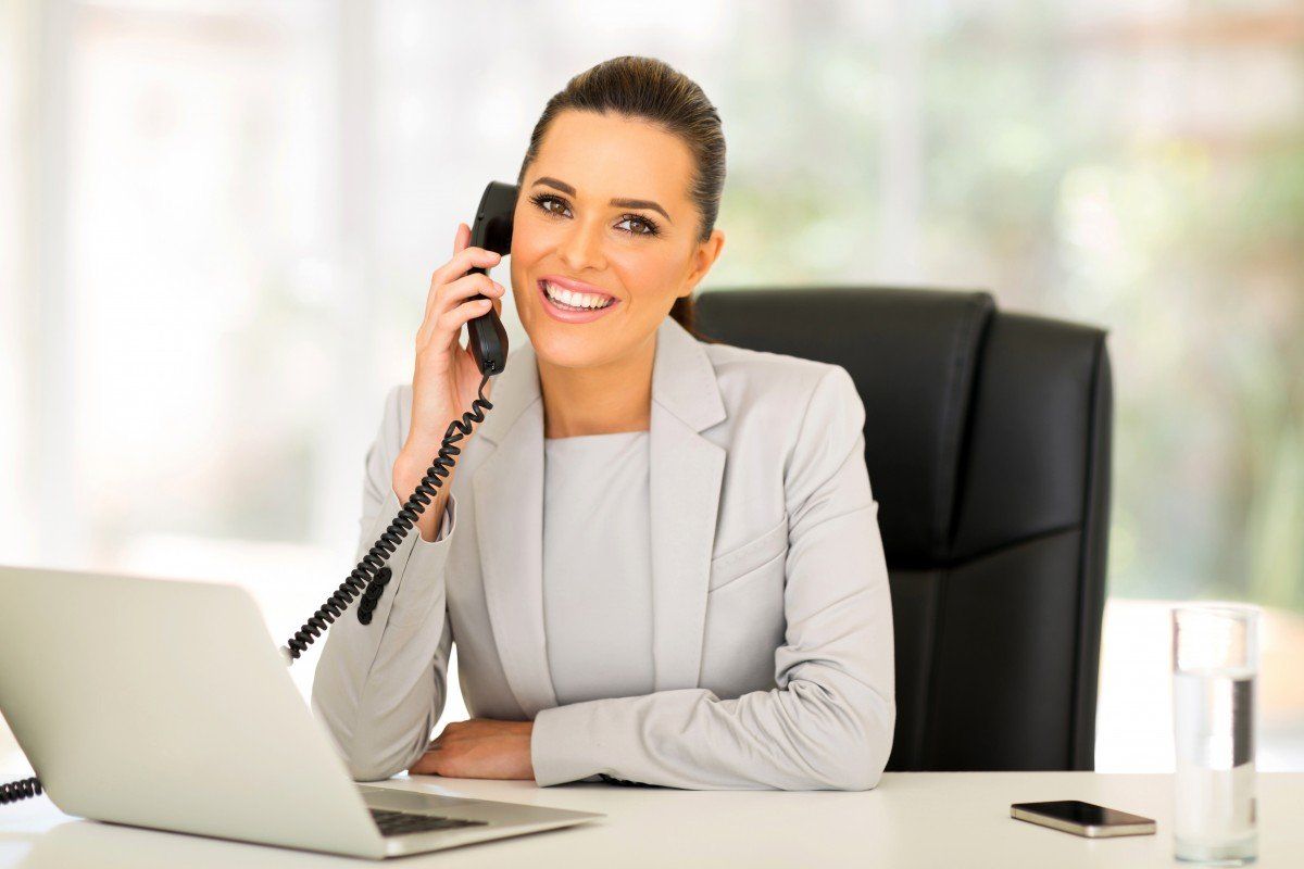 A woman is sitting at a desk talking on a phone.