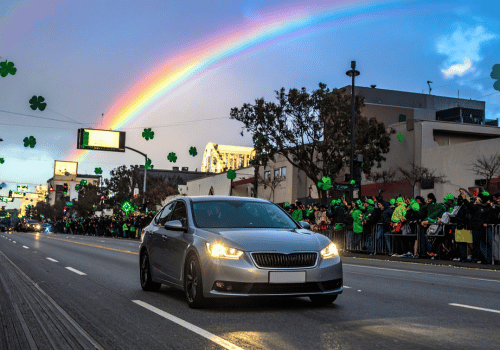 Sedan driving past a St. Patrick’s Day parade with a rainbow and shamrock graphics overhead.