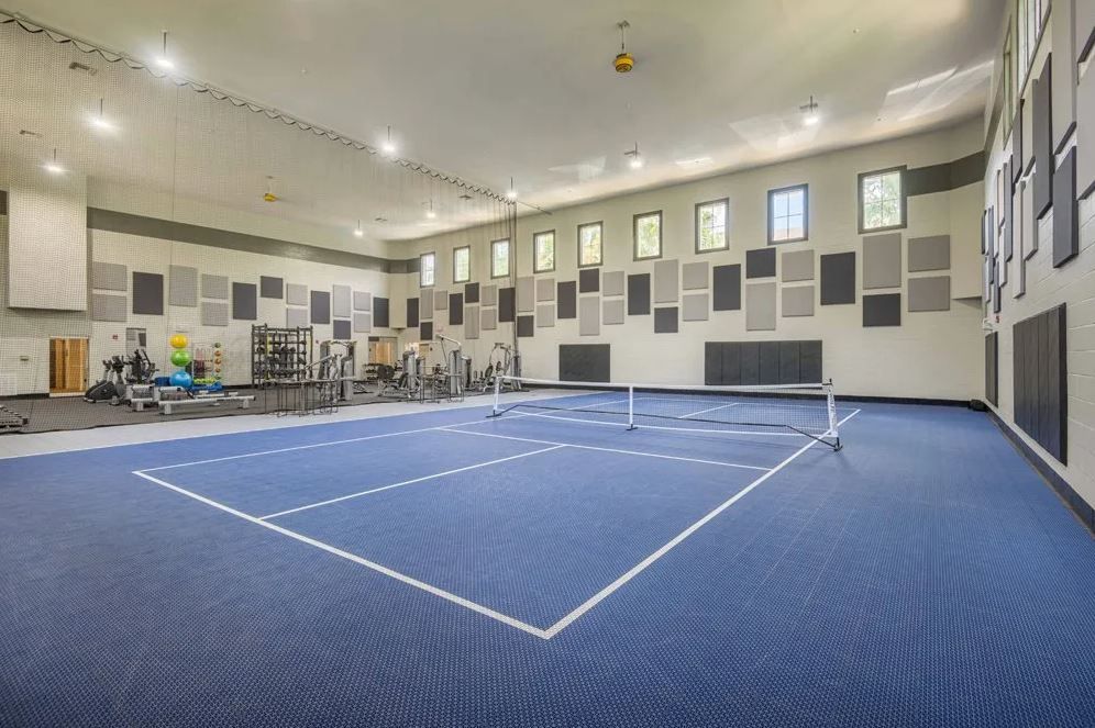 Indoor fitness center with a large blue court, a tennis net, and workout equipment along the walls.