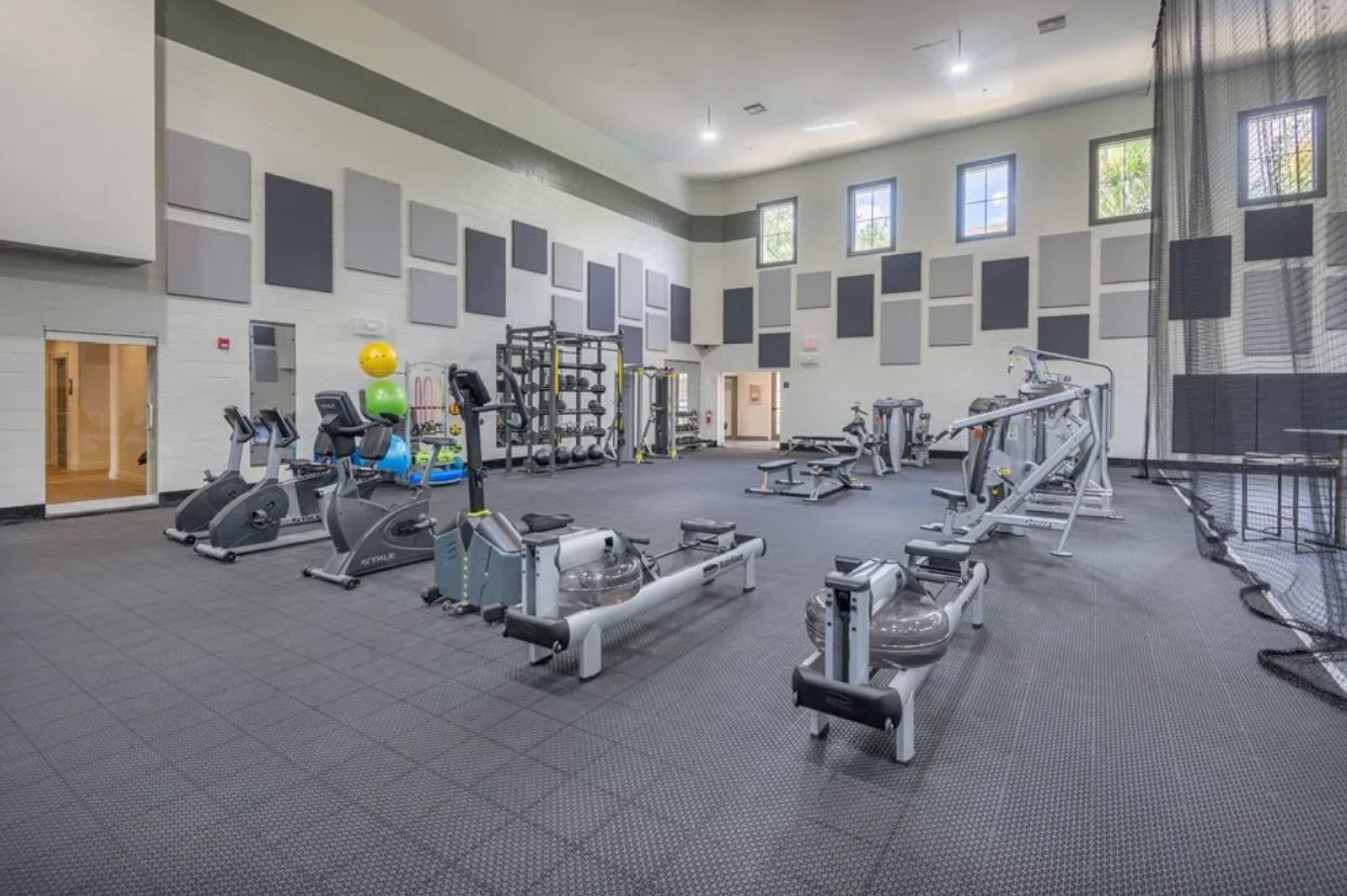 Interior of a modern community gym with cardio machines, weight racks, and group training area.