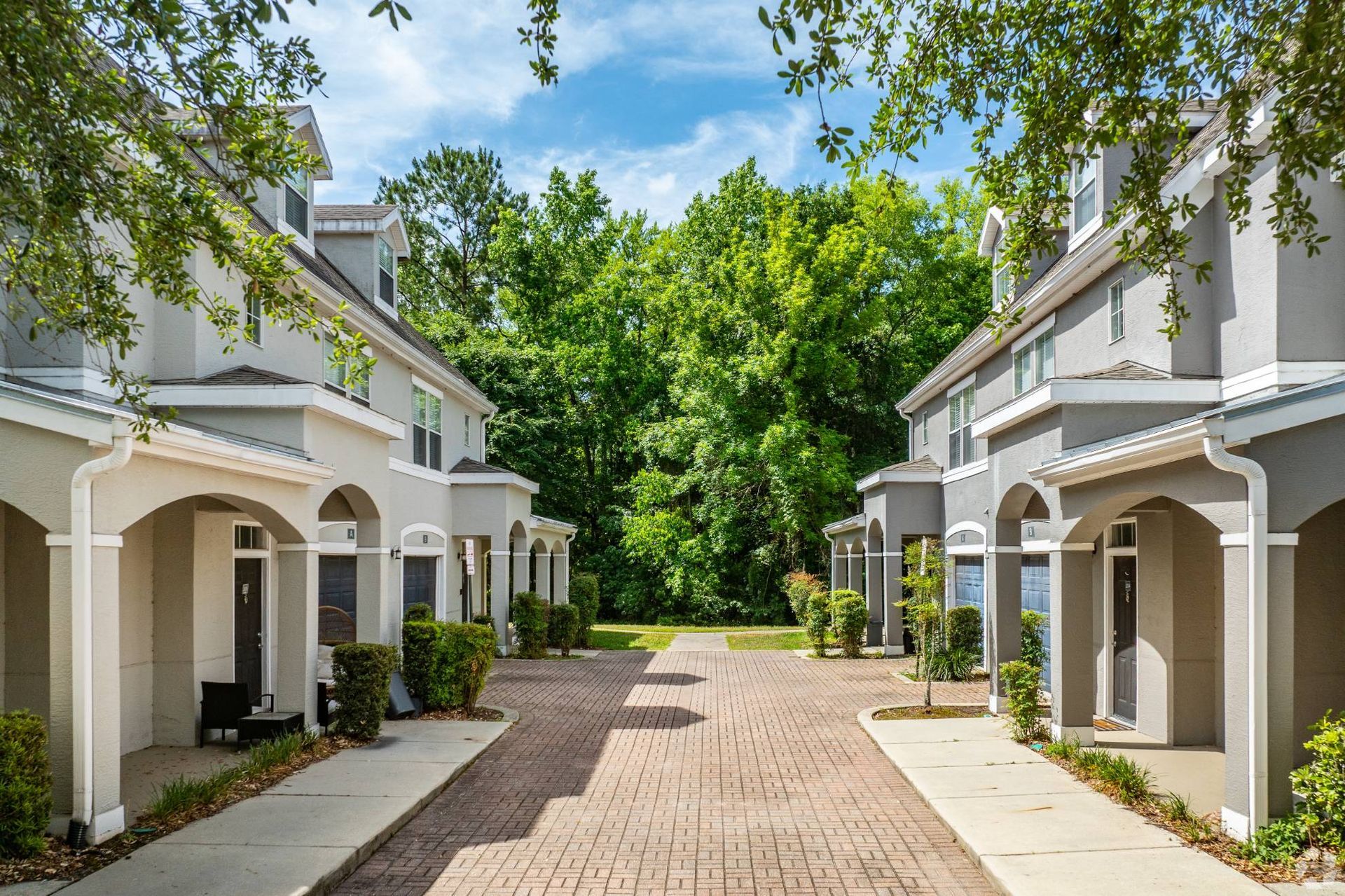 Exterior view of townhouse-style apartment buildings lining a brick courtyard with trees.