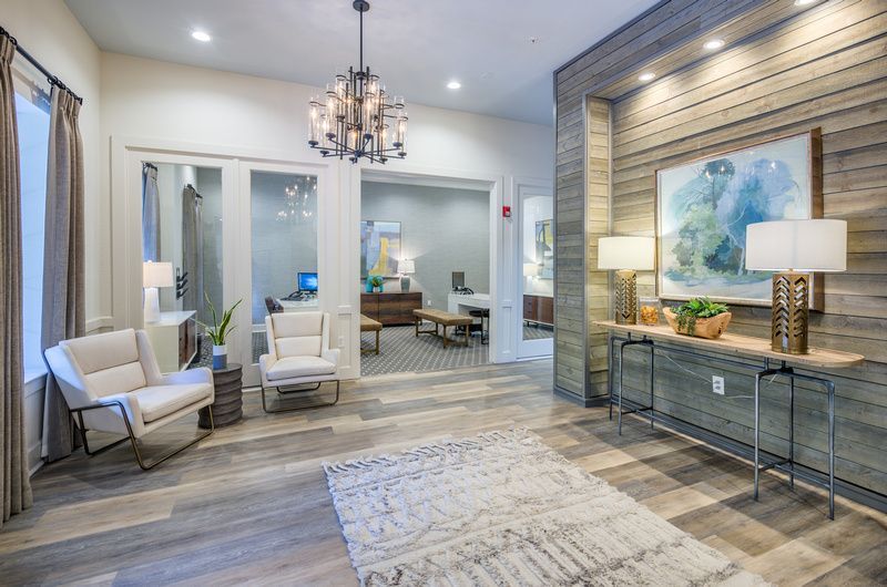 Modern apartment community lobby with white chairs, wood accent wall, and glass-front offices.