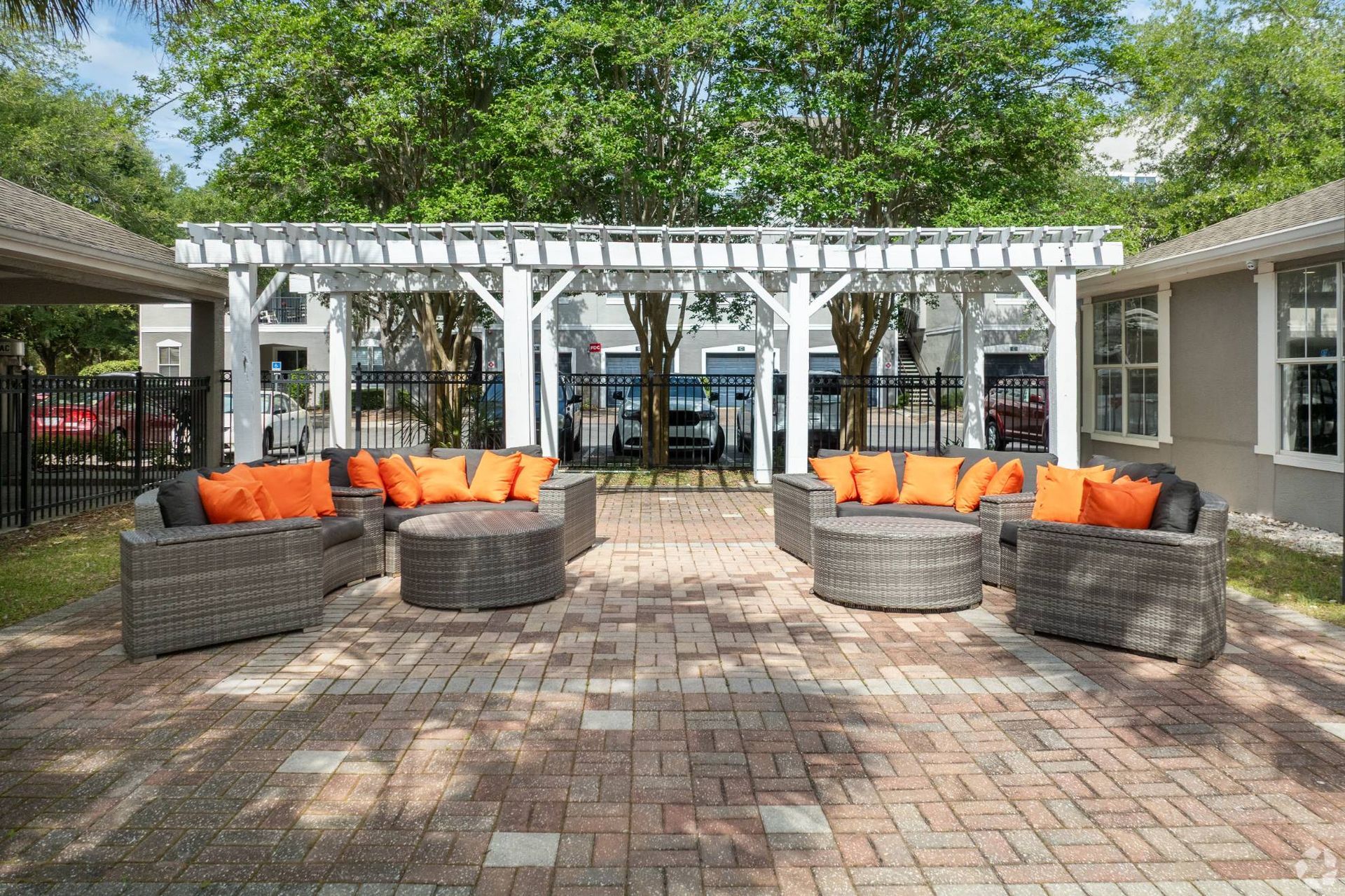 Outdoor community lounge with wicker seating and orange cushions under a white pergola.