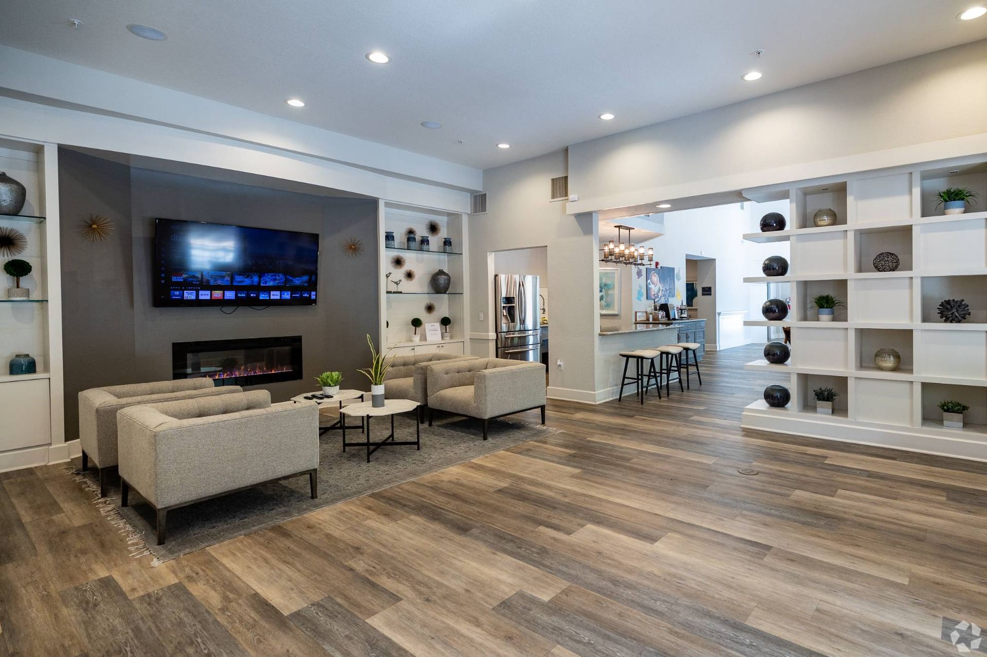 Modern resident lounge with couches, a wall-mounted TV, fireplace, and open kitchen.
