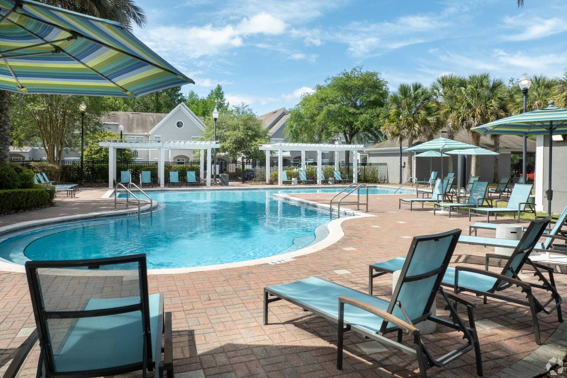 Outdoor apartment community pool with lounge chairs and striped umbrellas.