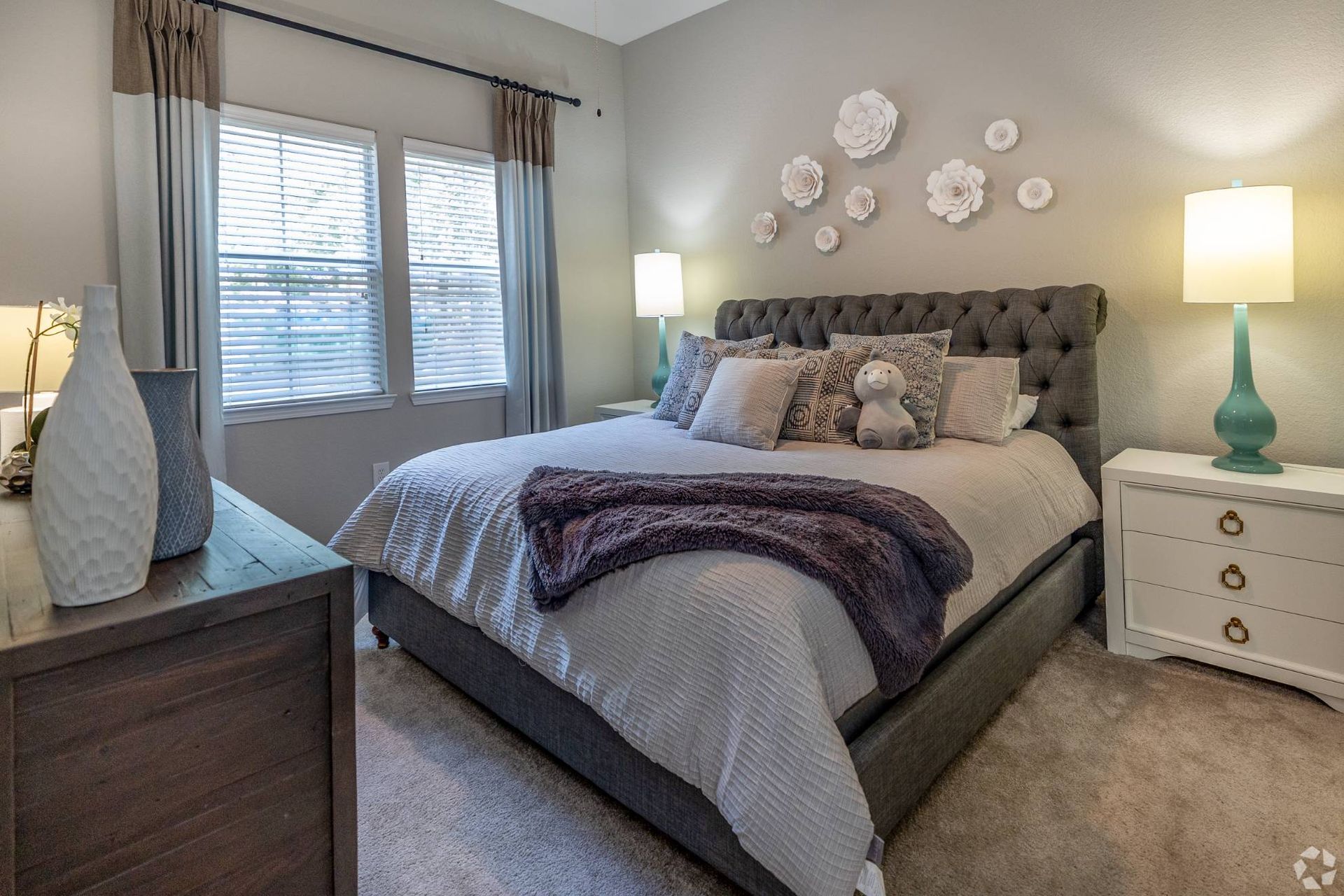 Bedroom in apartment with tufted headboard, two nightstands, lamps, and wall decor.
