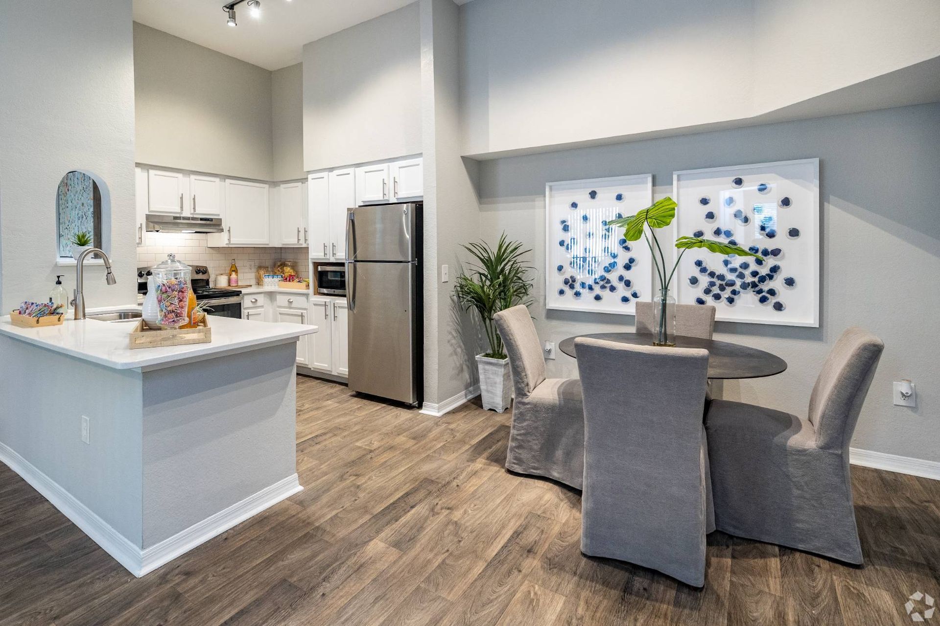Open-concept kitchen and dining area with white cabinets, stainless appliances, and two framed blue abstract art pieces.