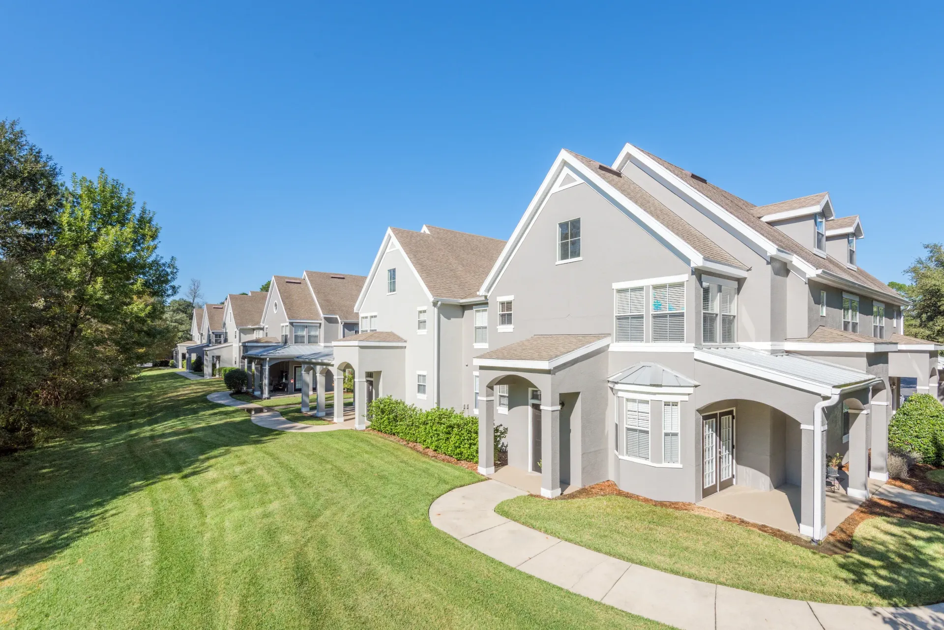 Row of townhome-style apartment buildings along a curved walkway with a green lawn.