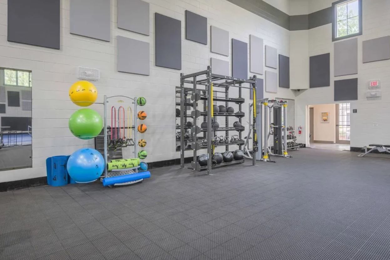 Modern community gym featuring a weight rack, medicine balls, stability balls, and mats.