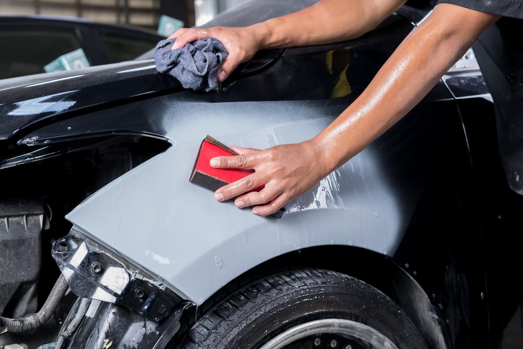 Mani che lucidano un pannello grigio di un'auto con una spugna rossa e un panno scuro