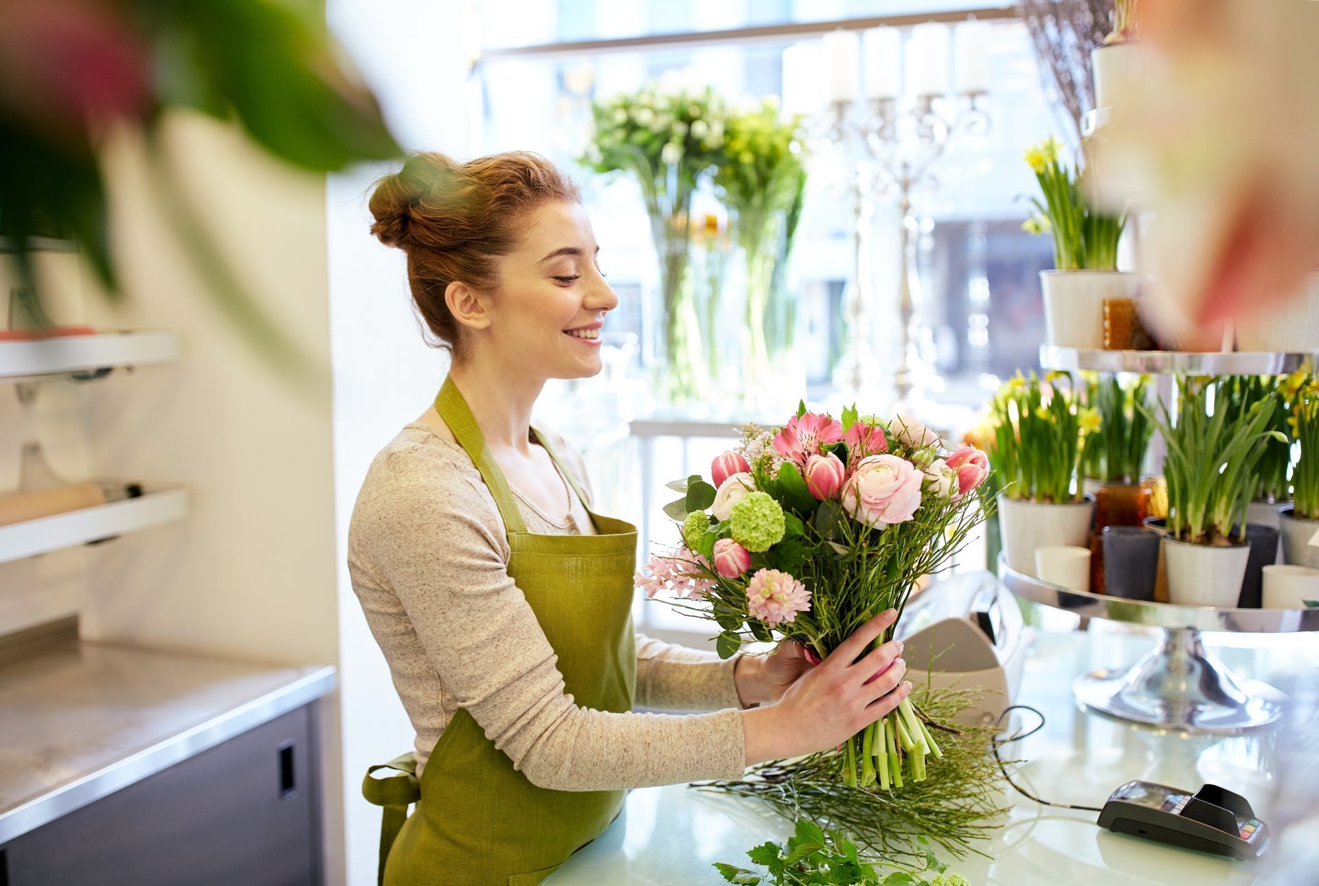 Florist crafts a bouquet of pink roses and green chrysanthemums in a bright, airy shop.