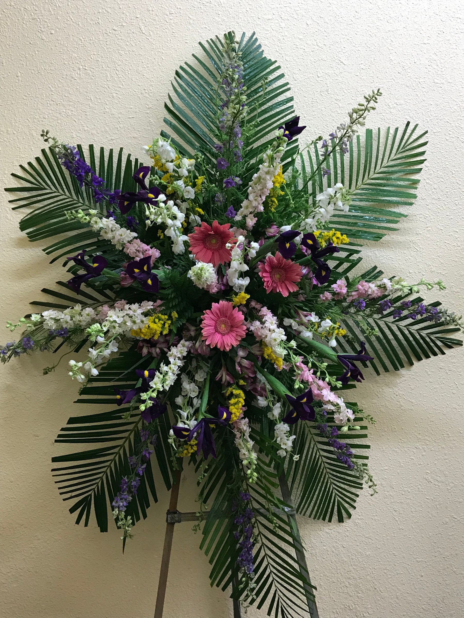 Standing funeral spray with pink gerberas, purple irises, and lush green palm leaves. Standing funeral spray with pink gerberas, purple irises, and lush green palm leaves.