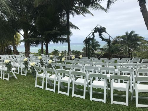 A Row Of White Folding Chairs Sitting On Top Of A Lush Green Field - Honolulu, HI - Bella Rosa Corporation