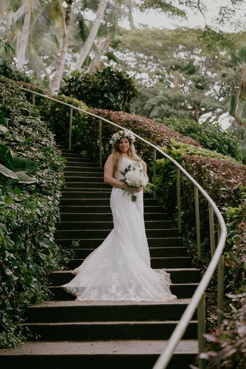A Bride In A Wedding Dress Is Standing On A Set Of Stairs Holding A Bouquet Of Flowers - Honolulu, HI - Bella Rosa Corporation