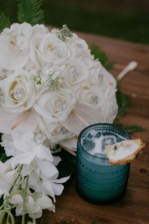 A Bouquet Of White Roses Is Sitting Next To A Blue Glass With A Drink In It - Honolulu, HI - Bella Rosa Corporation