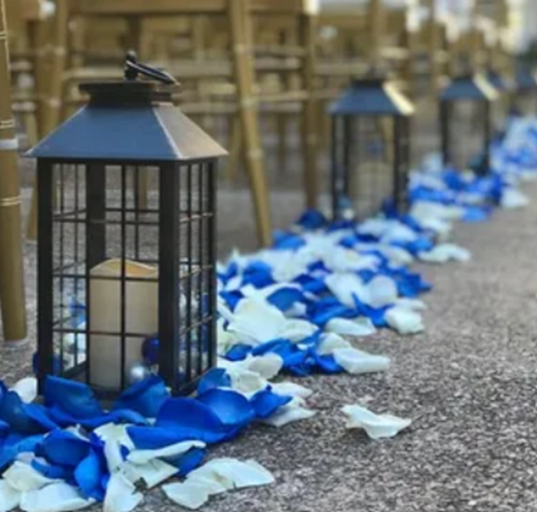 Black lanterns with white candles placed along an aisle decorated with blue and white rose petals.