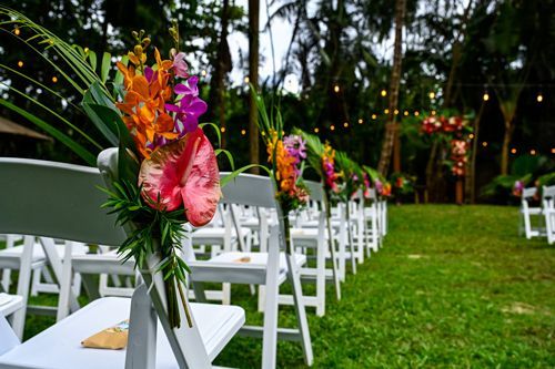 A Row Of White Folding Chairs Decorated With Flowers For A Wedding Ceremony - Honolulu, HI - Bella Rosa Corporation