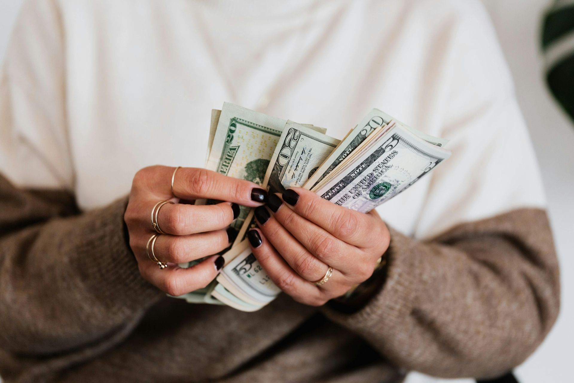 Hands holding several US dollar bills against a neutral background.