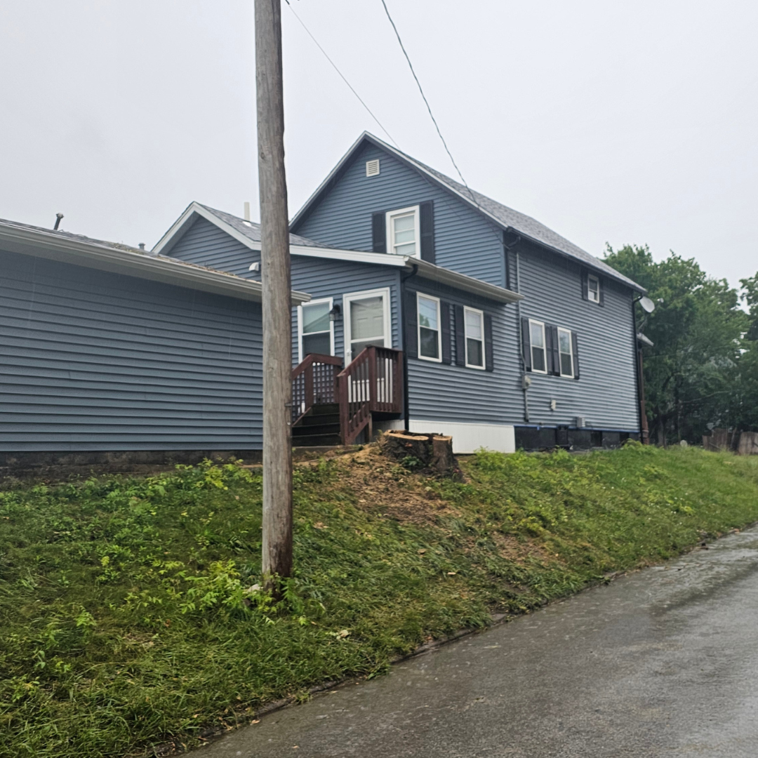 A large house is sitting on top of a grassy hill next to a street.