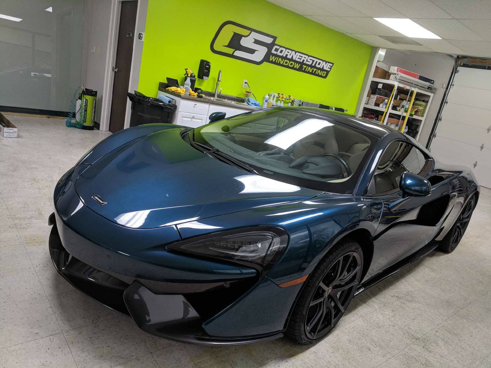 A blue sports car is parked in a garage in front of a green wall.