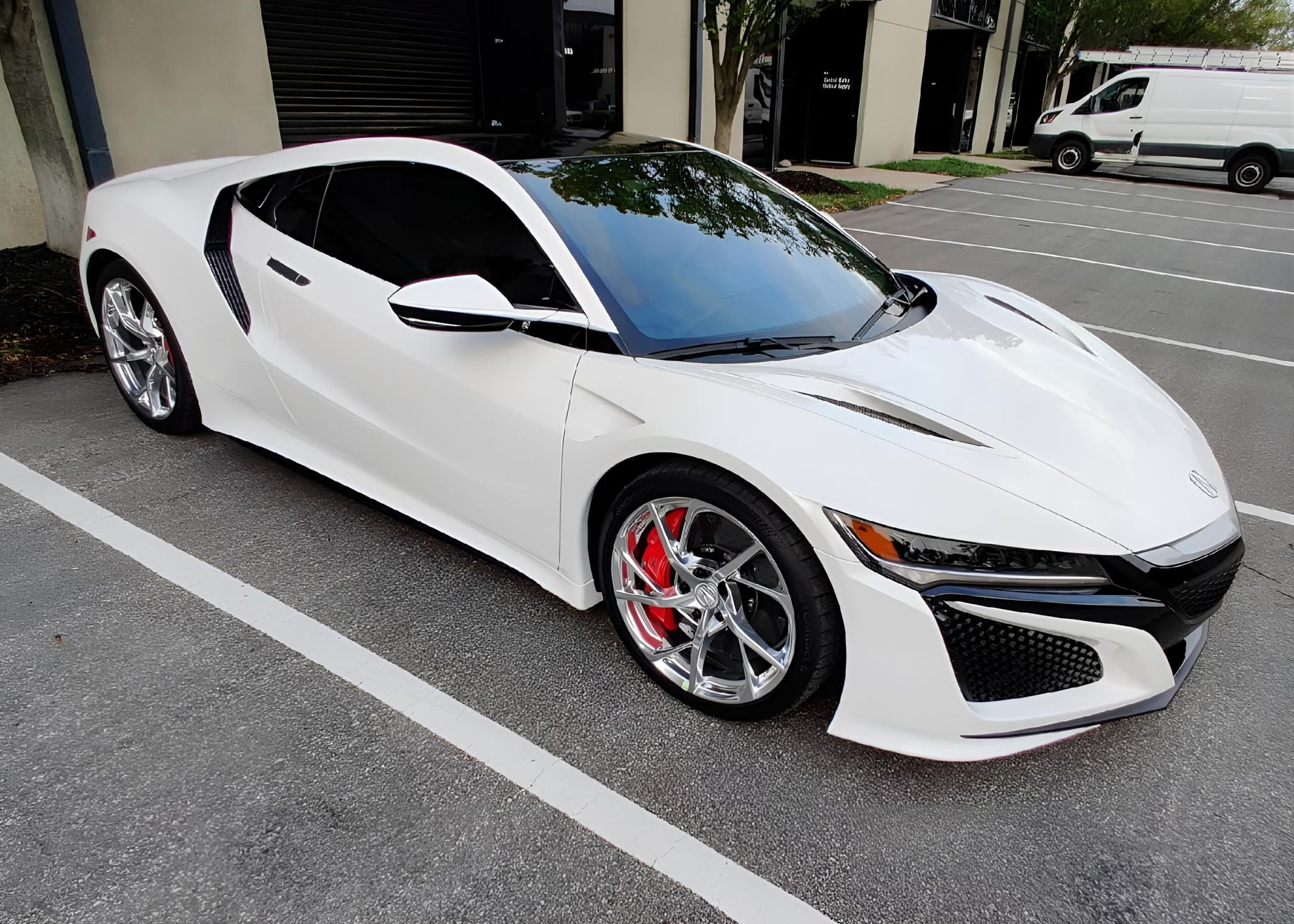 White Acura NSX sports car parked in front of a building, with tinted windows and chrome rims.