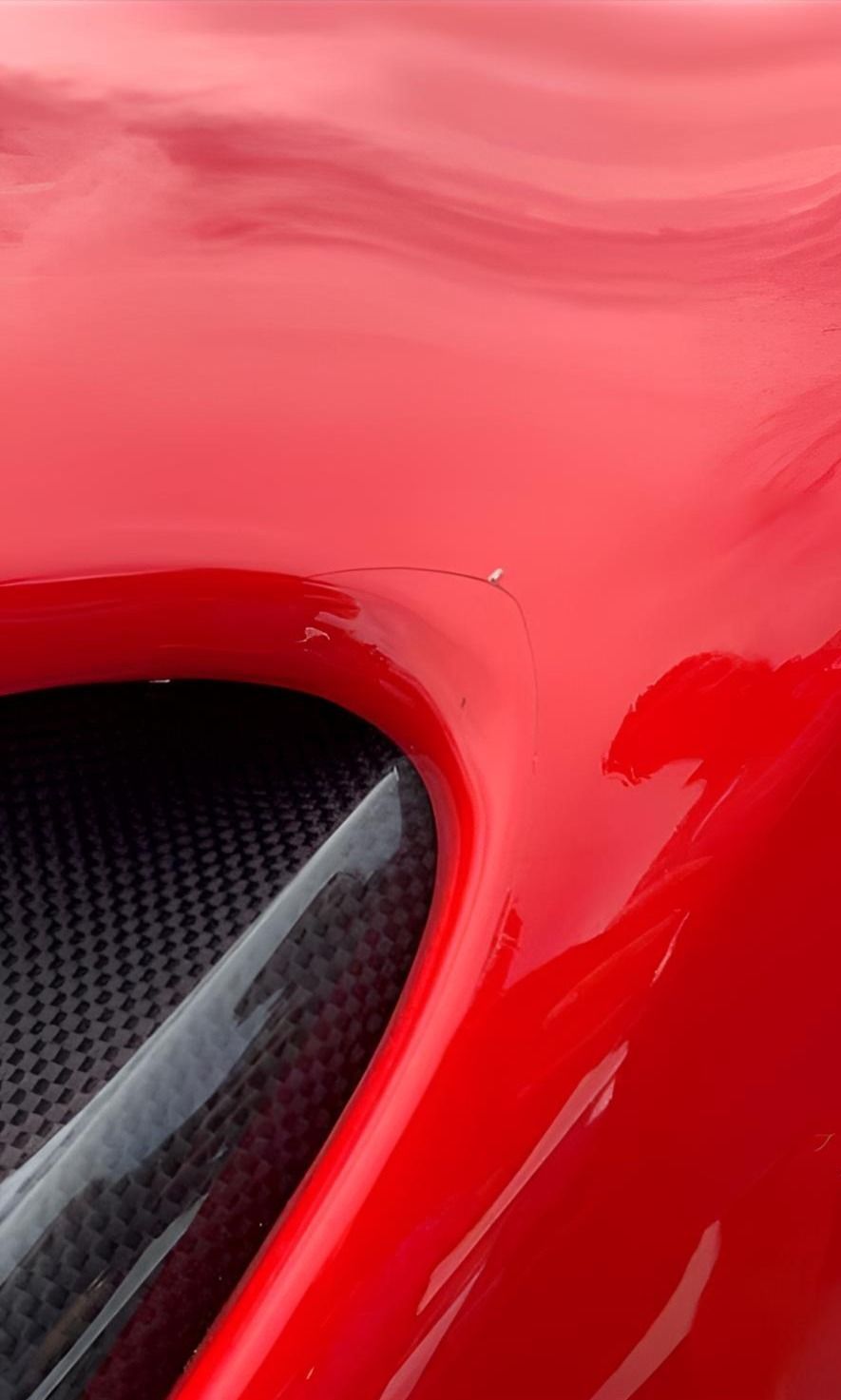 A close up of a red car hood with a carbon fiber grille.