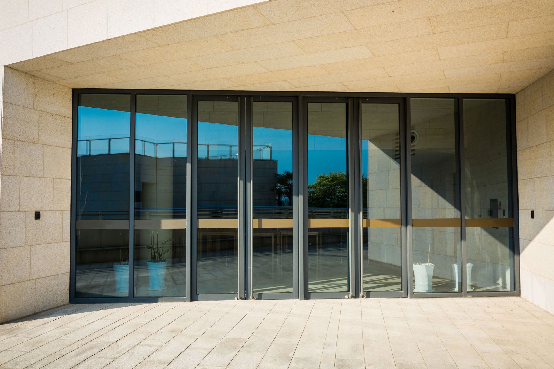 Glass folding doors on a modern building, reflecting sky and interior.