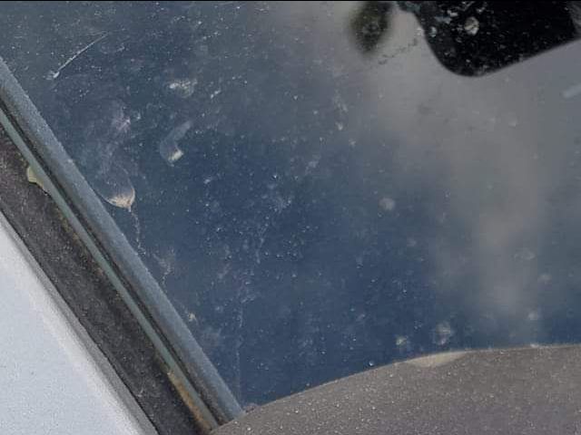 A close up of a dirty window with a reflection of a person in it.