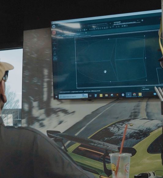 Man applying tinted film to a car window in a shop.
