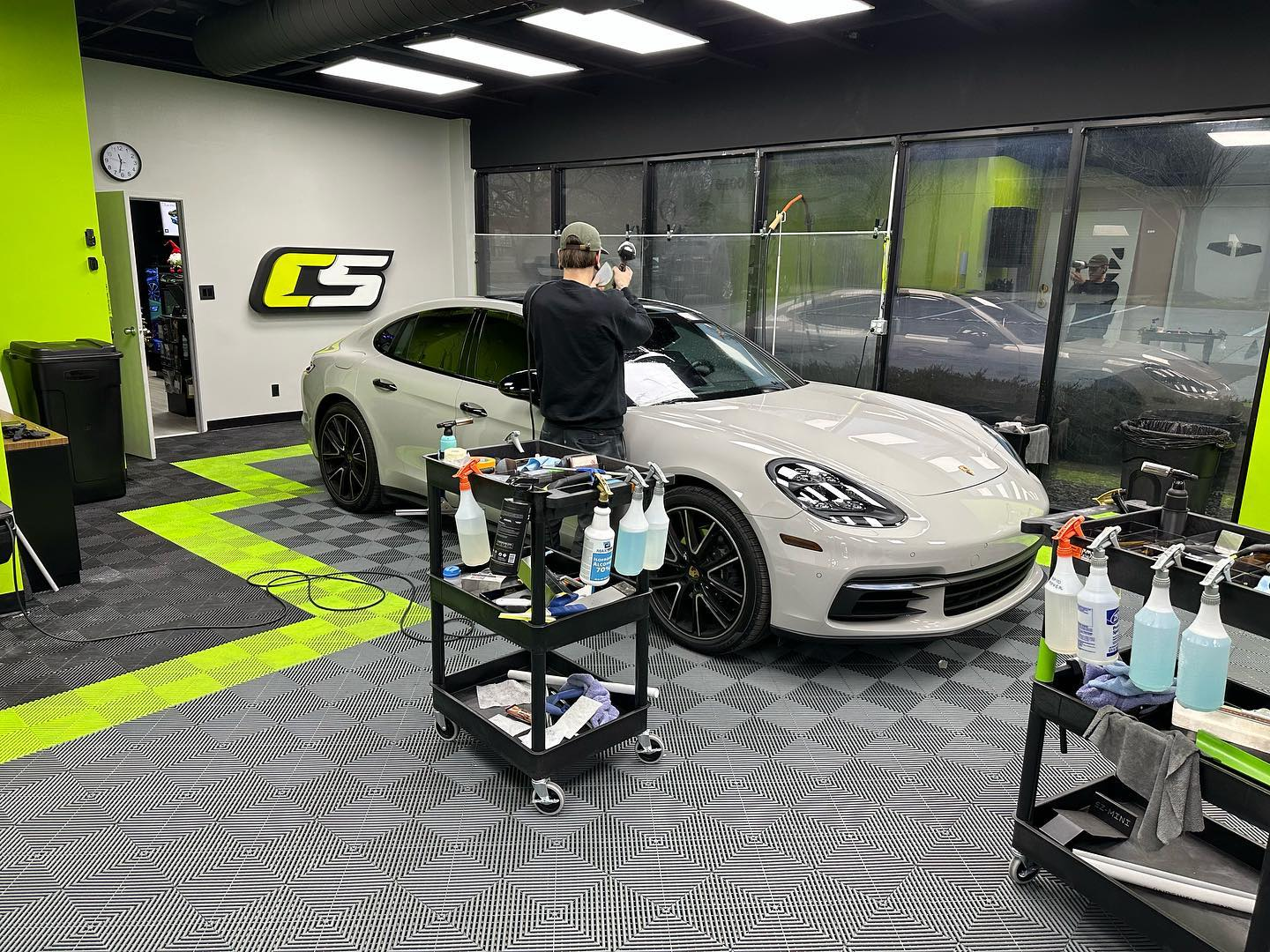 A person applying tint to a gray Porsche inside a car detailing shop.