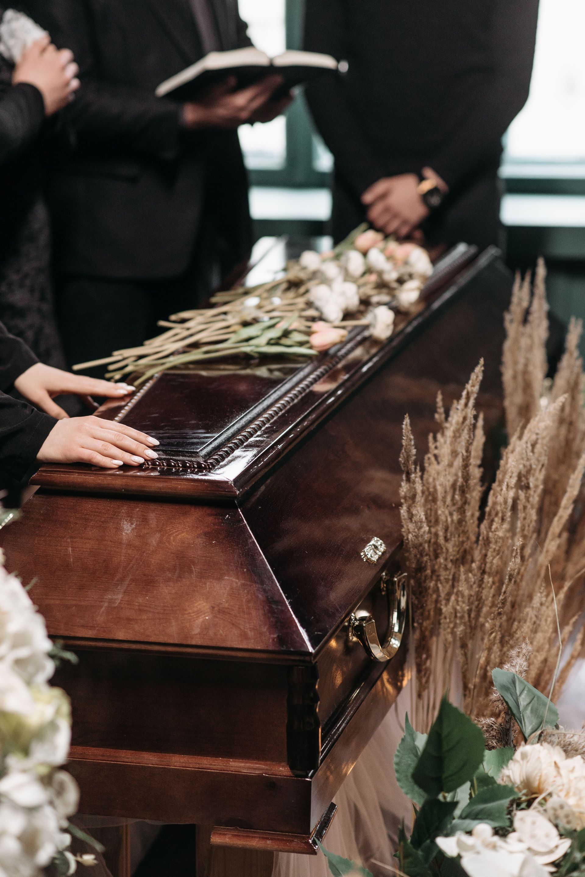 Bara aperta adornata di fiori durante una cerimonia funebre, con i partecipanti al lutto in piedi nelle vicinanze.