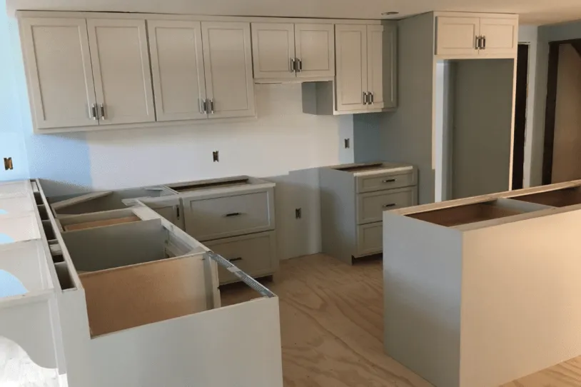 A kitchen with white cabinets and a wooden floor is being remodeled.