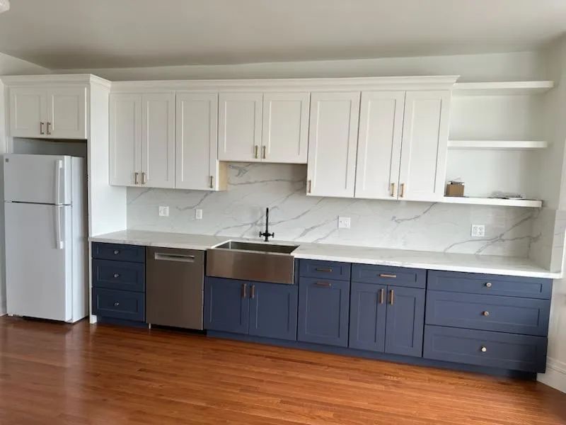 A kitchen with blue cabinets , white cabinets , a sink , and a refrigerator.