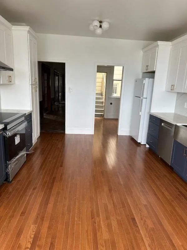 An empty kitchen with hardwood floors and white cabinets