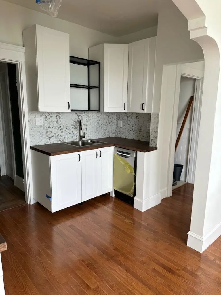 A kitchen with white cabinets , a sink , and a dishwasher.