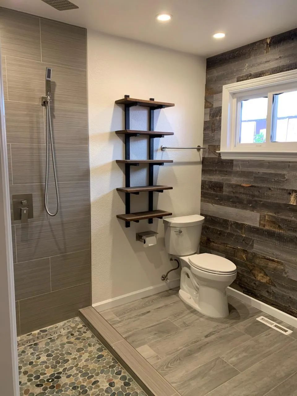 A bathroom with a toilet , shower and shelves.