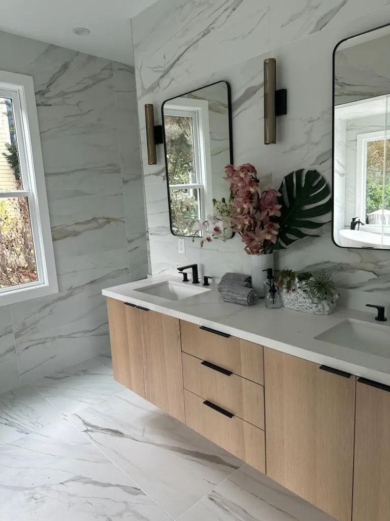 A bathroom with two sinks , two mirrors and a window.