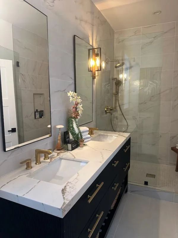 A bathroom with two sinks , a mirror and a walk in shower.