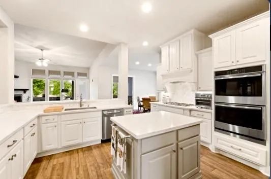 A kitchen with white cabinets , stainless steel appliances , and a large island.