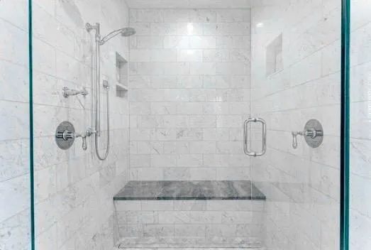 A bathroom with a walk in shower with a glass door and a bench.