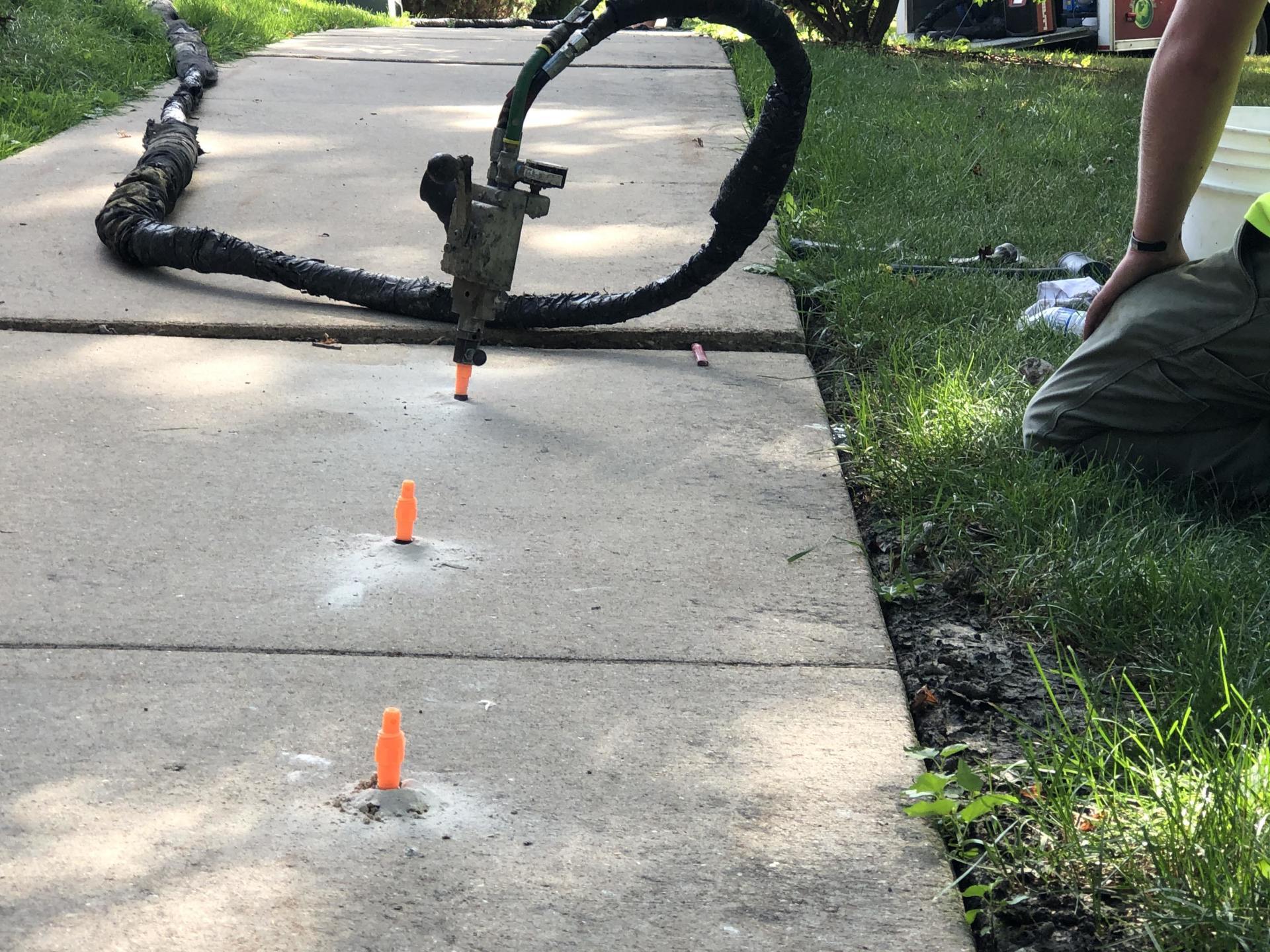 A person is kneeling down on a sidewalk with a hose attached to it.