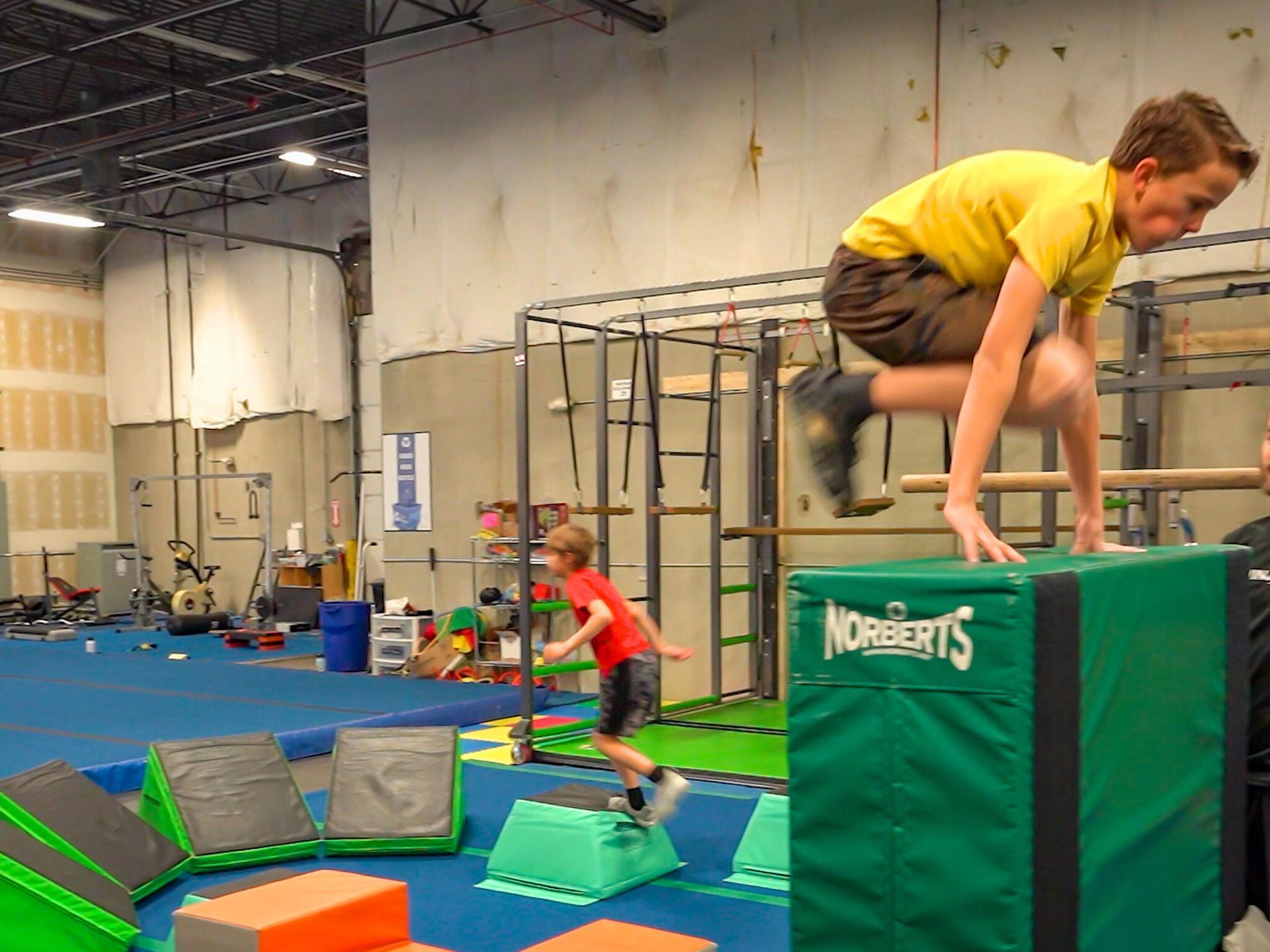 A man in a yellow shirt is jumping over a green block that says nobelarts